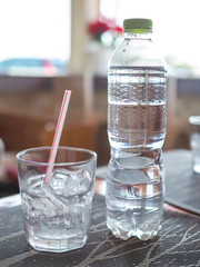 A glass​ which has ice and​ straw in​side​ and​ a plastic​ bottle​ on the table in...