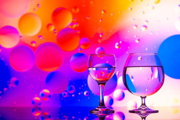 transparent glasses with water and oily drops on colorful background 
