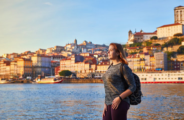 Fototapeta na wymiar Young woman tourist enjoying beautiful landscape view on the old town (Ribeira historical quarter) and river Duoro during the sunset in Porto city, Portugal