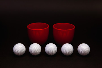 White golf balls and red cups of tea on the black table.