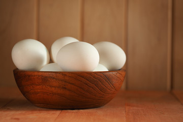 Chicken eggs in a wooden bowl on a wooden surface. Easter