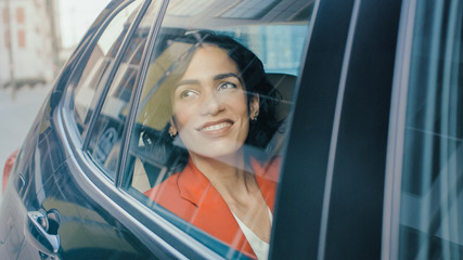 Beautiful Happy Woman Rides on a Passenger Back Seat of a Car, Looks out of the Window in Wonder. Big City View Reflects in the Window. Camera Mounted outside the Car. 