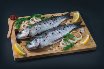 Grey mullet fish on the wooden board wıth lemon, onion and spices.
