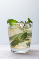 Glass with juice, ice and mint leaves on a white background. Refreshing cocktail.