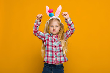 Portrait of cute little child girl with Easter bunny ears holding colorful eggs on yellow background. Happy easter