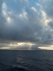 Sun rays burst out from behind clouds over the ocean