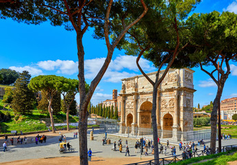 Triumphal Arch in ancient Rome Italy. Ancient vintage landmark. Famous monument near roman Coliseum. Summer area with green trees and tourists people. Sunny day with blue sky and clouds.