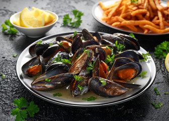 Mussels with white wine, garlic, lemon and herbs in a plate, French fries. rustick background. Seafood.