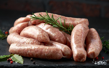 Freshly made raw butchers sausages in skins with herbs on stone board