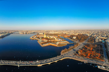 Fototapeta premium Beautifull aerial view of the Petropavlovsky fortress in sunny spring day. Golden tall spire of famous Peter and Paul Cathedral on the blue sky background. Historical centre of St. Petersburg, Russia.