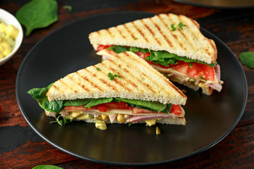 Sandwich with ham, cheese, tomatoes, spinach, corn, mayonnaise, mustard, gherkins, toasted bread and potato chips.