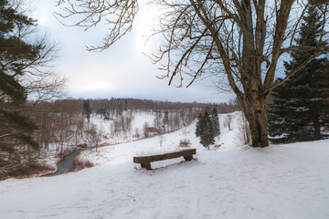 A wooden bench at the edge of a hill covered by the snow. Toila park, Estonia.
