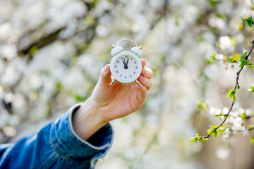 Female hand holding alarm clock near flowering tree