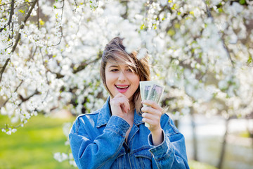 girl in a denim jacket and money stands near a flowering tree