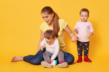 Tired merry woman plays with her active funny kids being on maternity leave. A young cheerful woman enjoys spending time within the family circle, keeps her children together. Childcare concept.