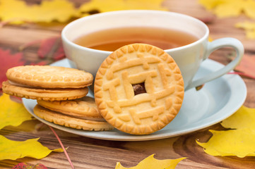 Cup of tea with cookies on the table with autumn leaves.