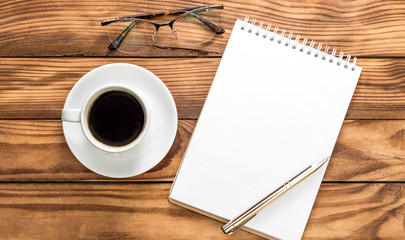 Blank notepad with eyeglasses nad cup of coffee on the table. Top view.