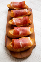 Crostini with serrano ham on rustic wooden board, low angle view. Close-up.