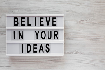 Top view, 'Believe in your ideas' words on lightbox over white wooden background. Flat lay, from above, overhead. Copy space.