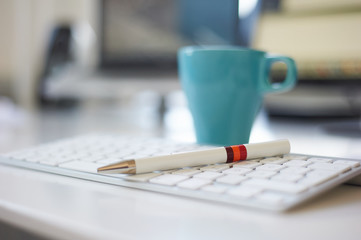 Kugelschreiber mit orange und roter Banderole liegt auf einer weißen Tastatur vor einer hellblauen...