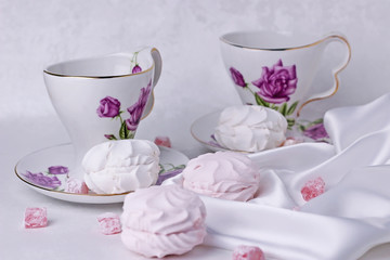 White and pink marshmallows are on the table with beautiful cups for tea.