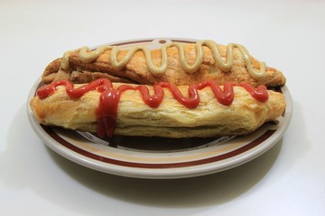 Closeup view of two sausage rolls in a plate with mustard and ketchup isolated on a white table