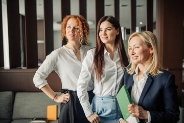 Portrait of three caucasian business women with different hairstyle, dressed in formal wear posing in a hotel lobby