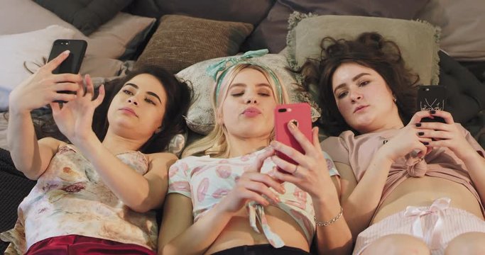 Attractive teenager ladies using smartphone while laying down on the bed and eating a bubble gum , wearing pajamas and texting someone s and taking selfies. shot on red epic. 4k