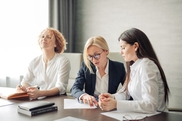 Three caucasian female students or interns in white shirts , intern using laptop, working on pc, studying in university, typing, browsing websites, apps, writing report, chatting in social network