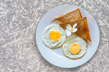 Fried eggs with toast on a white plate decorated with a tropical flower. Delicious healthy breakfast at a tropical resort