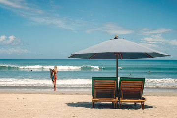 Beach umbrella with deck chairs against the ocean with surfers