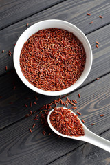 red rice in a ceramic bowl with spoon against dark wooden background