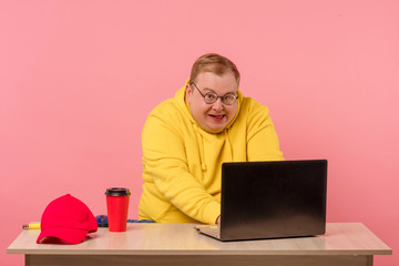 Funny plump man geek in yellow sweatshirt having foolish face expression using laptop with funny...