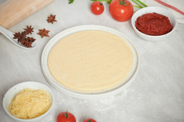 Fresh dough pizza base and ingredients on a white table. Top view.