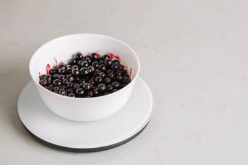 Fototapeta na wymiar Black currants in a white ceramic bowl is on a kitchen scale. Top view. Ripe and tasty currants on a linen tablecloth.