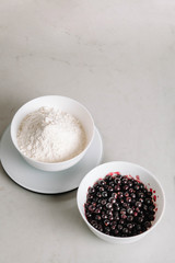 Flour and black currant Ingredients for baking. Top view, close-up. Black currant and sugar in a bowls in white
