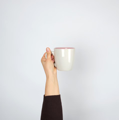gray ceramic cup in female hand on a white background, hand raised up