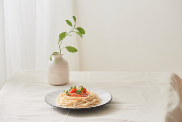 Food, spaghetti bolognese sauce in white dish and a vase of plants on a white prepared table