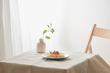 Food, spaghetti bolognese sauce in white dish and a vase of plants on a white prepared table