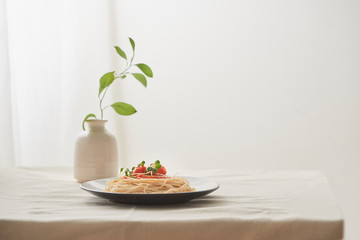 Food, spaghetti bolognese sauce in white dish and a vase of plants on a white prepared table