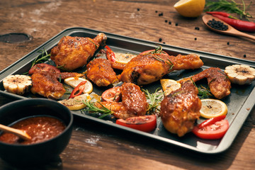 Grilled chicken drumstick and wings on baking tray over wooden table