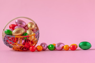 Sweet Easter candy eggs in basket on pink background.