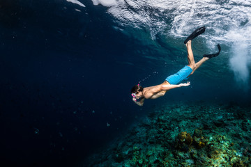 Young man snorkeling and skin diving over the coral reef edge in the tropical sea - obrazy, fototapety, plakaty