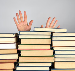 a stack of different books on a gray background, two female hands