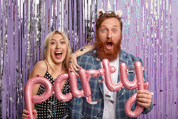 Oh no, what giant party we organized! Surprised happy young woman and man have housewarming celebration, invite many friends, pose in festive clothes with letter shaped balloons. Entertainment