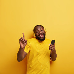 Happy unshaven black man drags to rhythm of music, listens popular song in headphones, connected to...