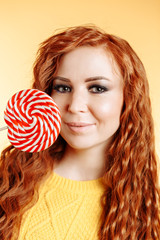 Beautiful curly redhead woman holding a red white lollipop and smiling.