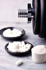 Creatine and Taurine capsules, Scoop of Whey Protein and a dumbbell. Bodybuilding food supplements on stone / wooden background. Close up. Copy space.