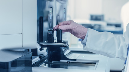 Close-up Female Research Scientist's Hand Places Test Tube with Blood Sample Into Medical Analyzing Equipment. Scientist Works in Modern Pharmaceutical Laboratory