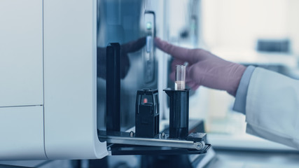 Close-up Female Research Scientist's Hand Pushes the Button for Starting Analyzing Blood Samples in Test Tubes in Medical Analyzing Equipment. Scientist Works in Modern Pharmaceutical Laboratory.